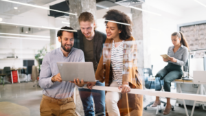 Employees gather around a laptop in an office environment.