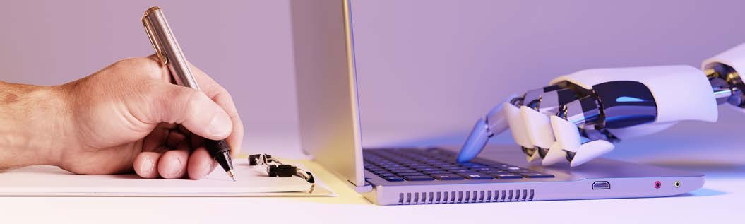 A human hand writing beside a robotic hand using a laptop.